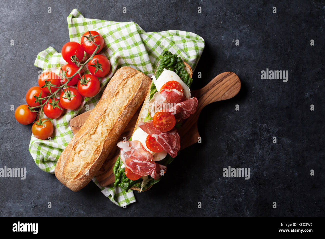 Ciabatta sandwich with romaine salad, prosciutto and mozzarella cheese over stone background