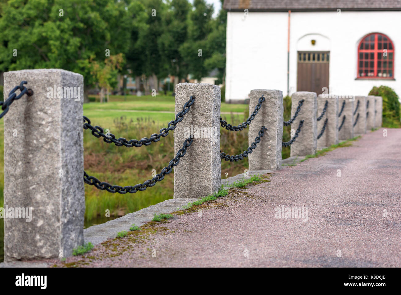 Stone pillars and iron chain as railing along road. Church in background. Stock Photo