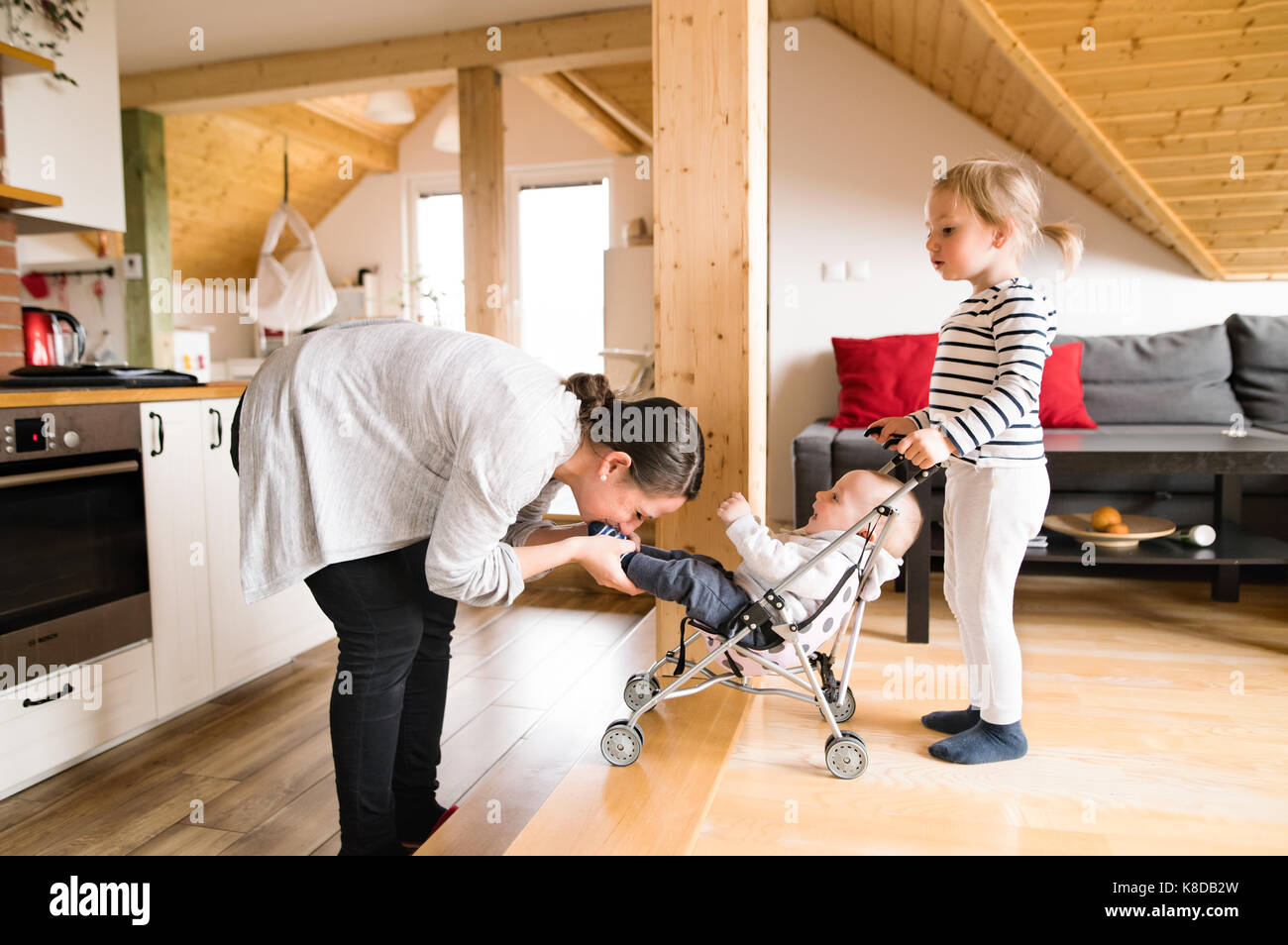 Girl with baby brother in toy stroller at home with mother. Stock Photo