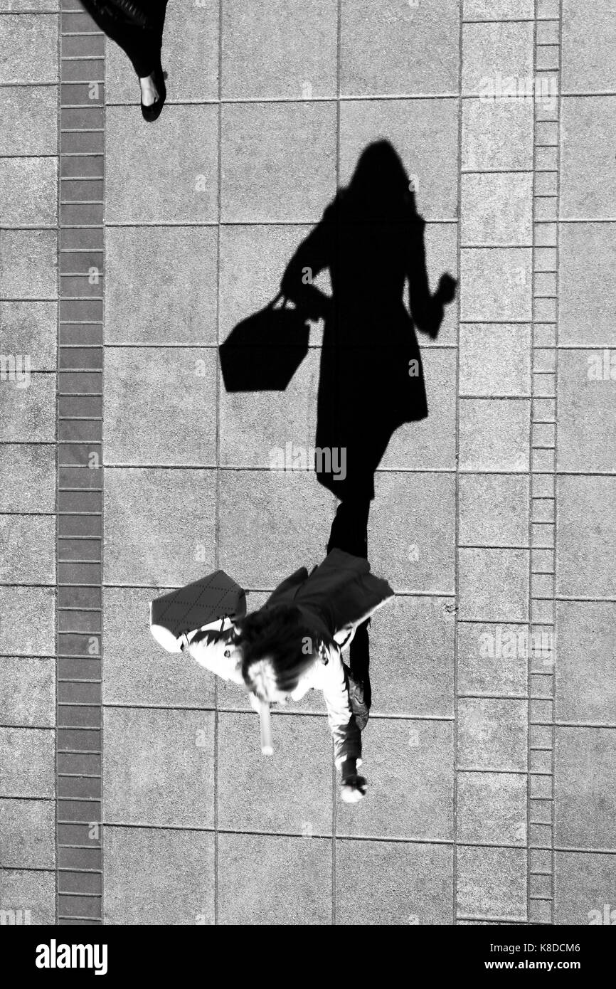 Shadow of a woman , walking and holding a purse , on city sidewalk from above in black and white Stock Photo