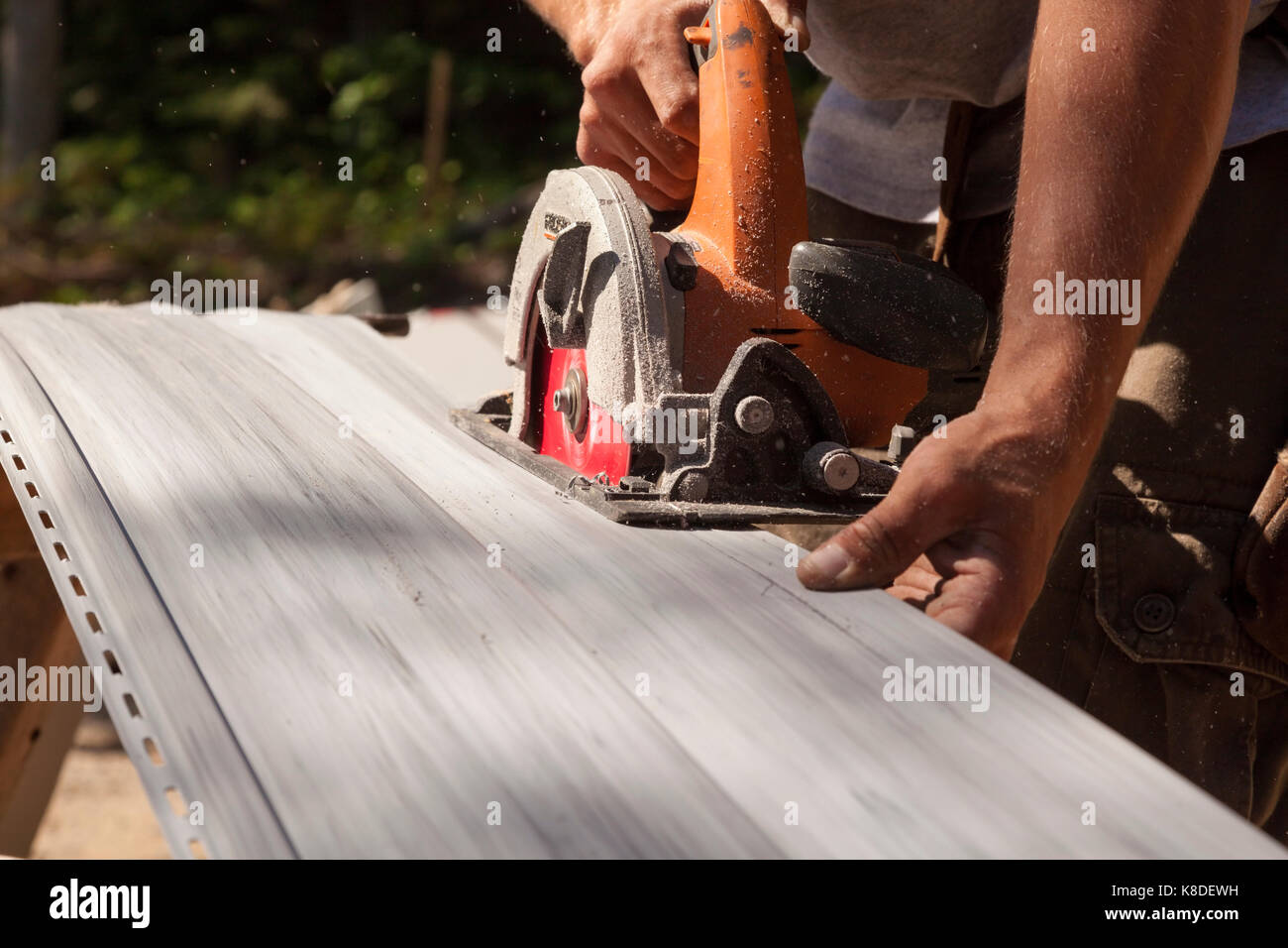 A construction worker using a handheld circular saw to cut through vinyl siding in Ontario, Canada. Stock Photo