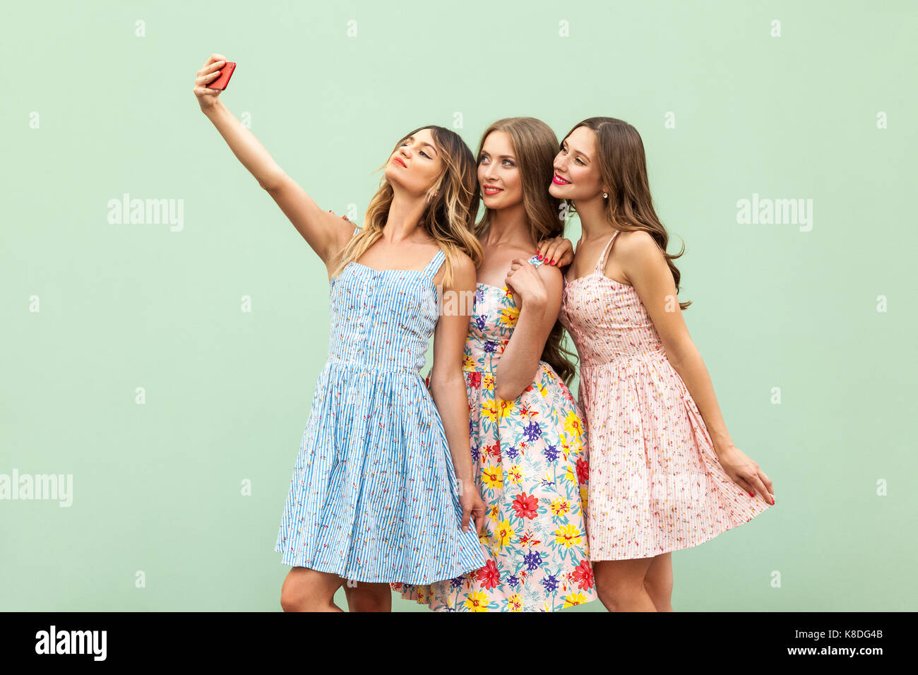 Hipsters three friends in casual dress, macking selfie on green background and have fun. Studio shot Stock Photo