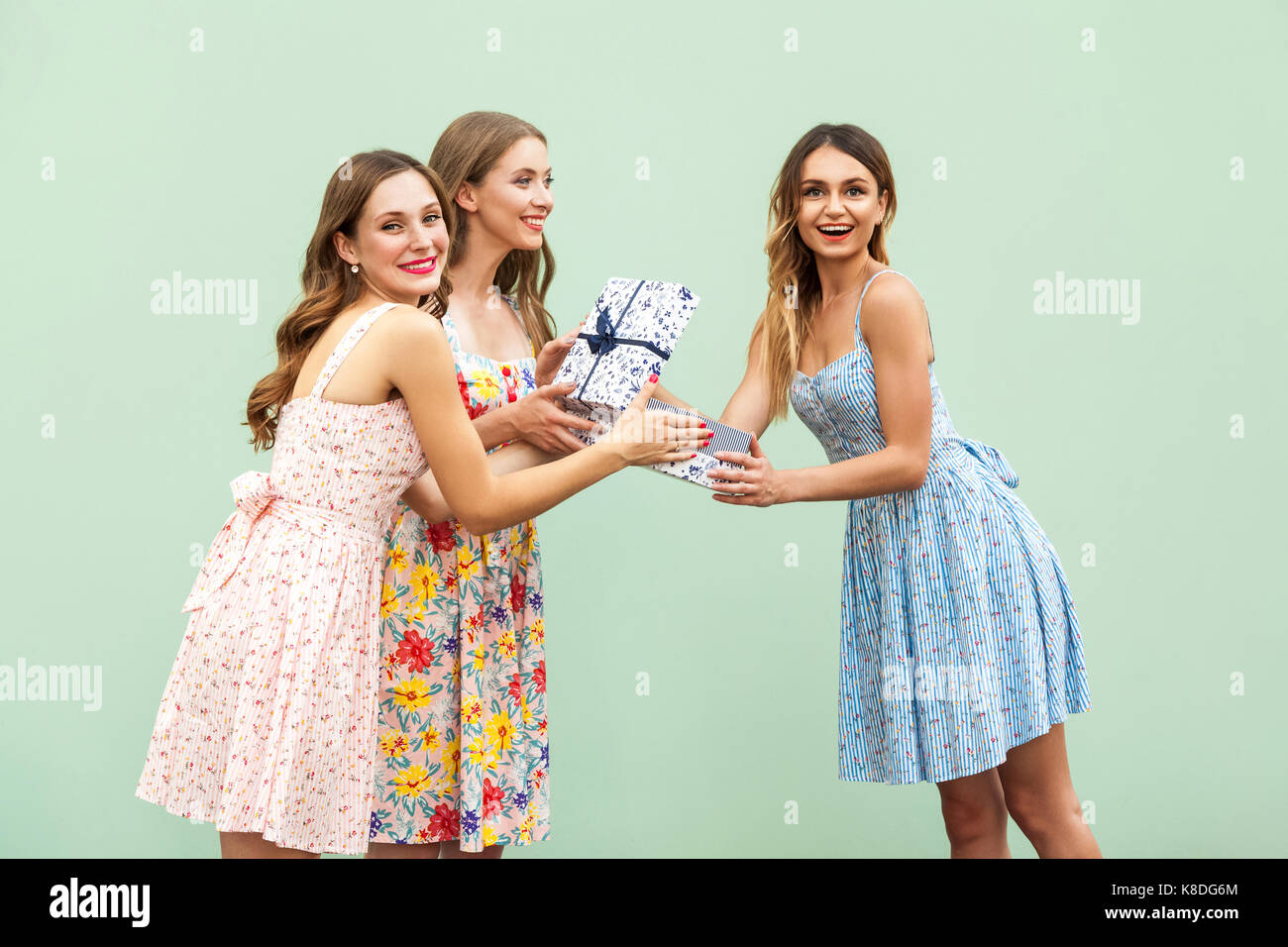 Portrait of surprised young adult woman in dress opens a presents box from her friends, isolated on green background, studio shot Stock Photo