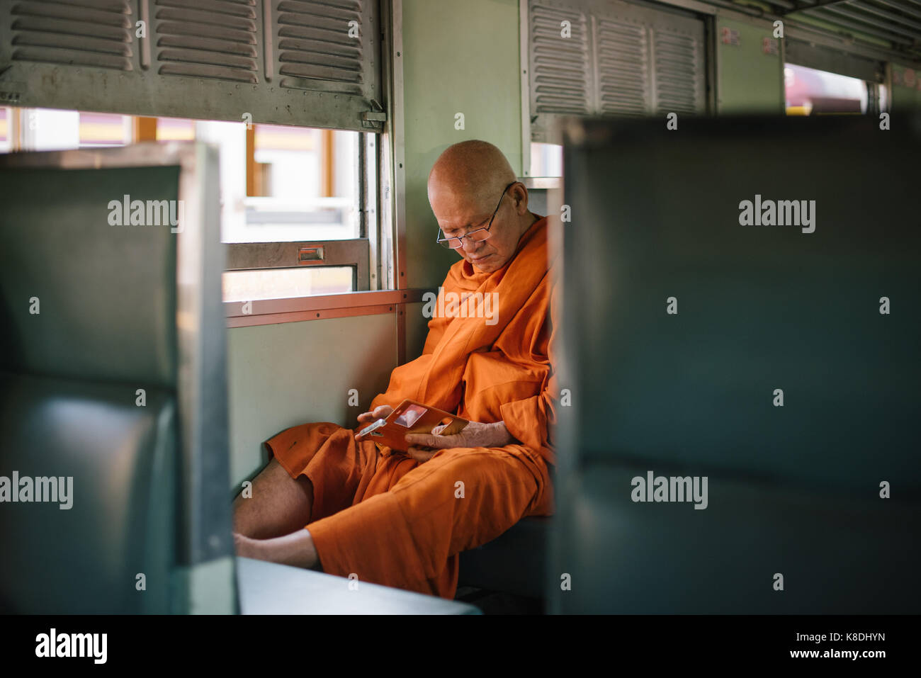 Modern Monk using his smartphone on a train in Bangkok, Thailand Stock Photo