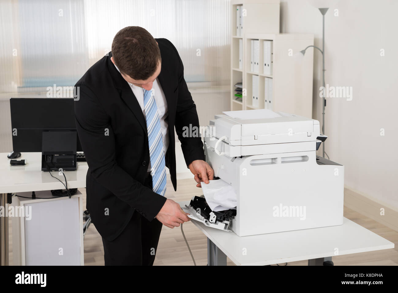 Mid adult businessman removing paper stuck in printer at office Stock