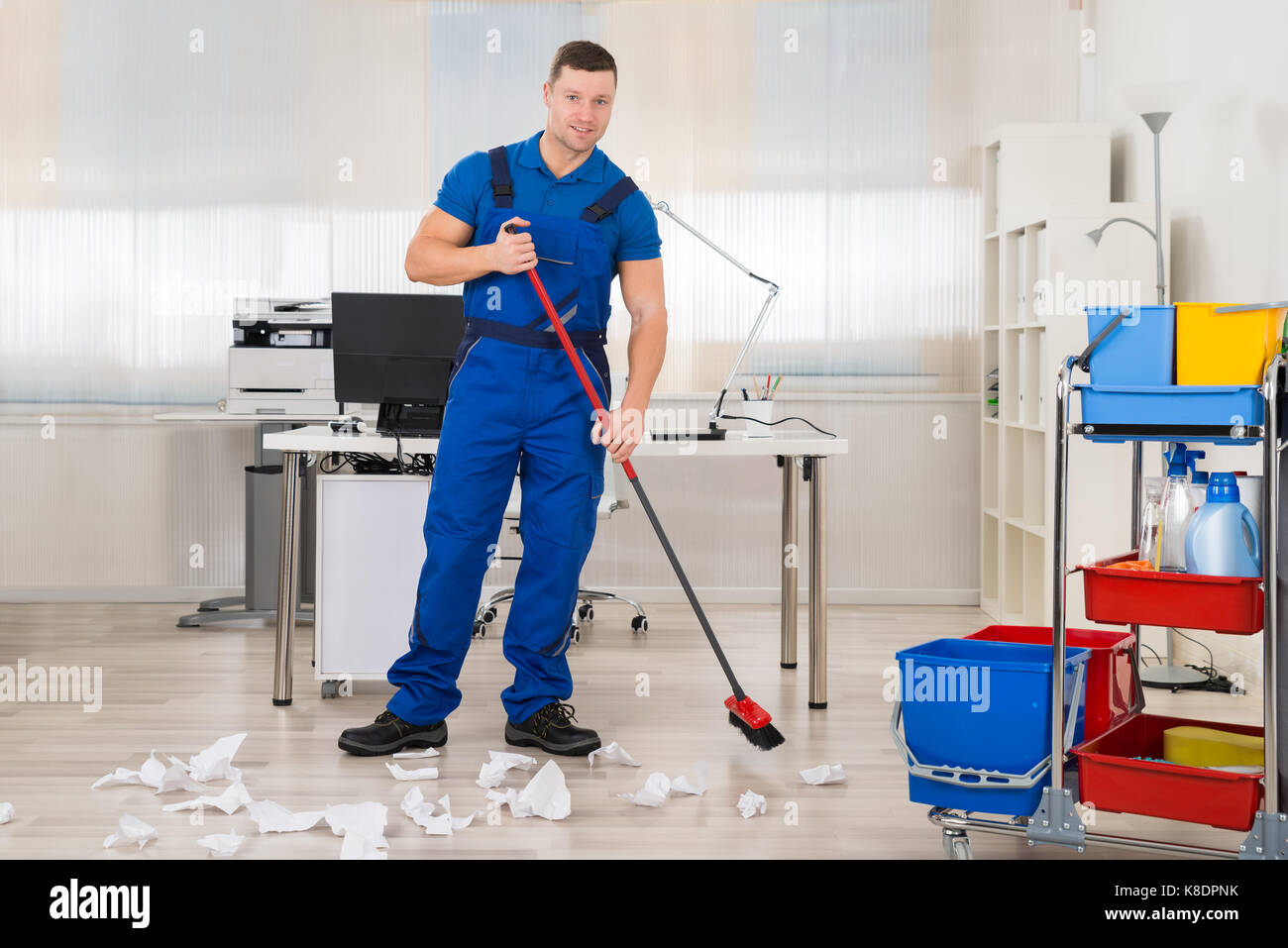 Full length of male janitor cleaning floor with broom in office Stock
