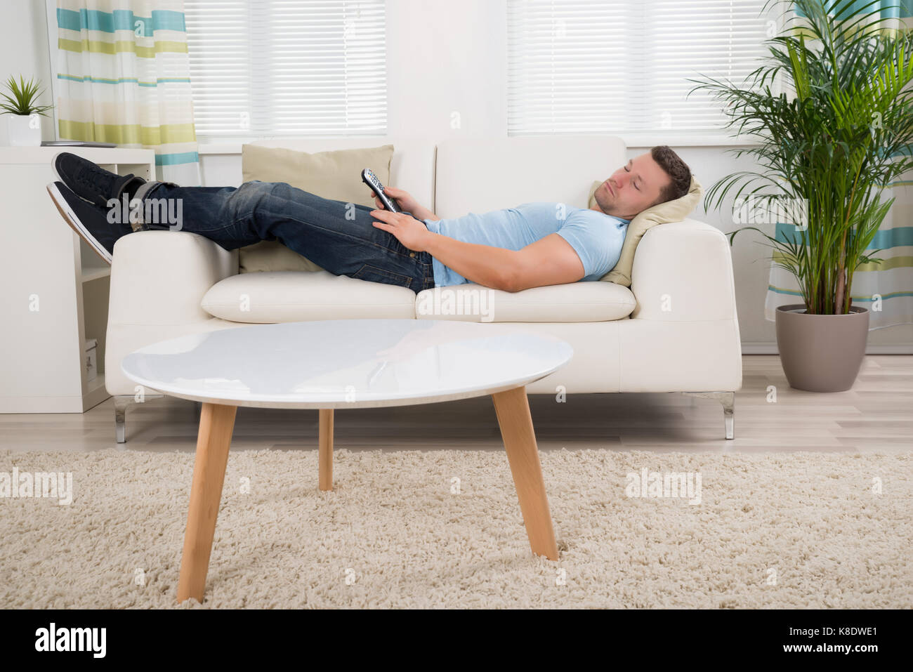 Full length of mid adult man with remote control sleeping on sofa at home Stock Photo