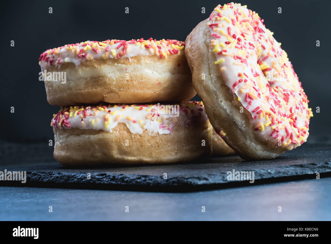 Three donuts stacked on a piece of slate. Stock Photo