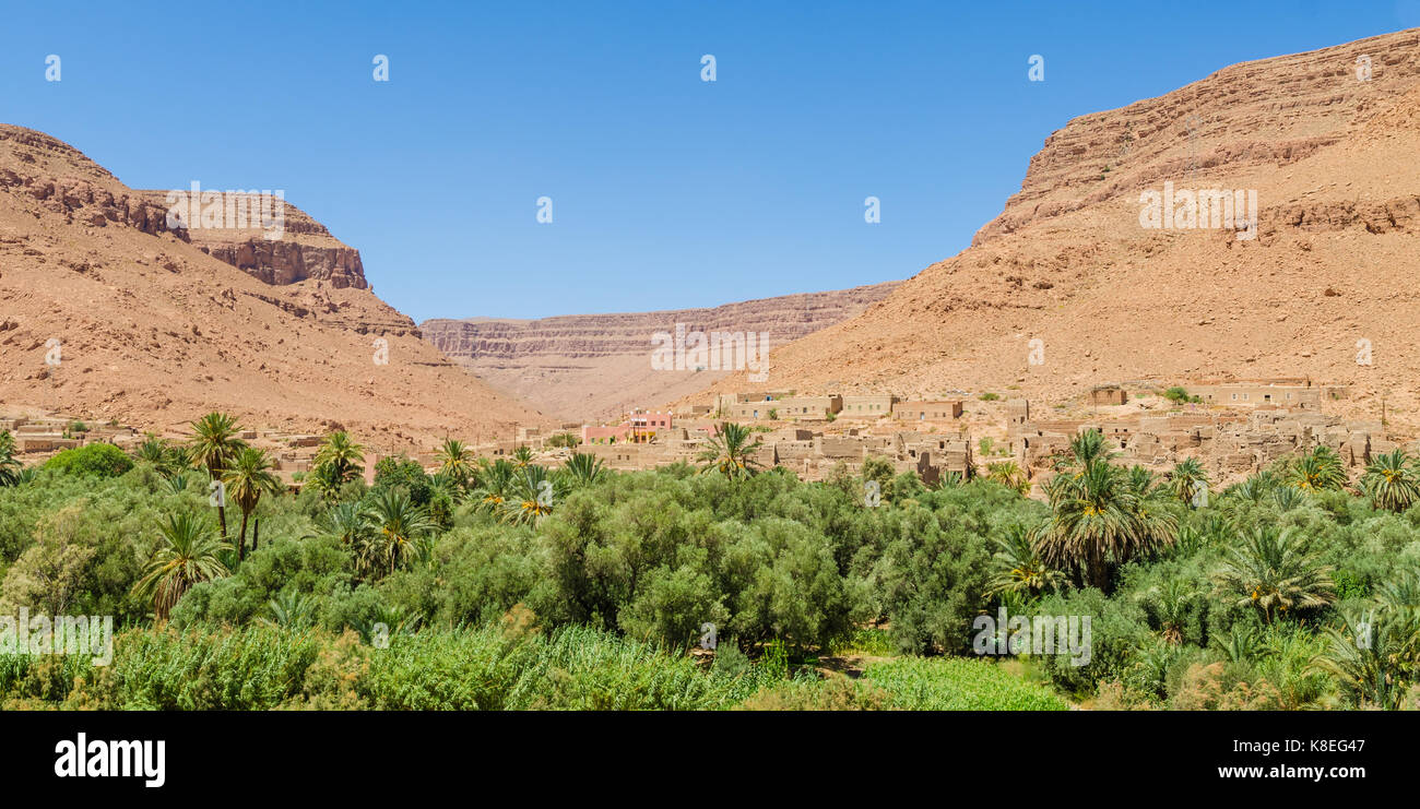 Moroccan clay village perched between orange mountains with palm tree oasis in front, Morocco, North Africa. Stock Photo