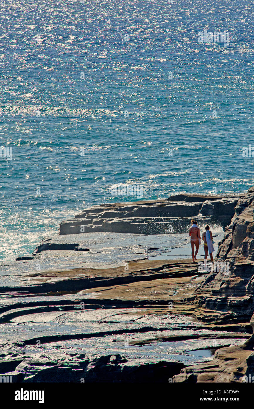 Two persons walking on the rugged ocean shore on a bright sunny day near Honolulu, Hawaii Stock Photo