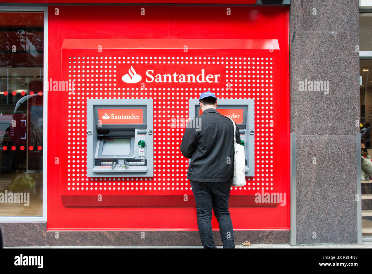 A young man standing in front of an ATM on Tottenham Court Road, London, UK Stock Photo
