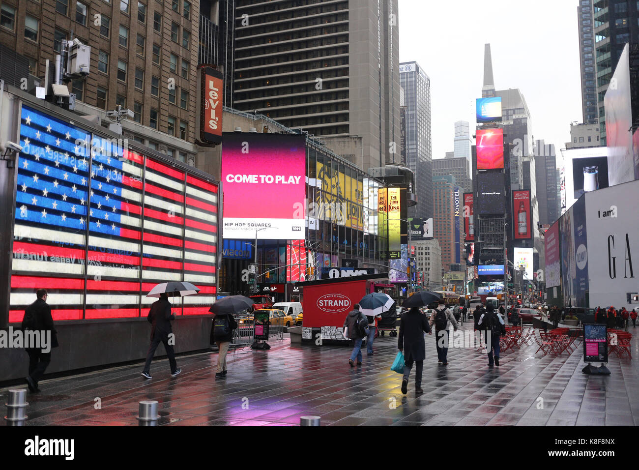 NEW YORK, USA - MARCH 2017 - View of Times Square on a rainy day, the american flag is shown at the side on an electronic panel Stock Photo