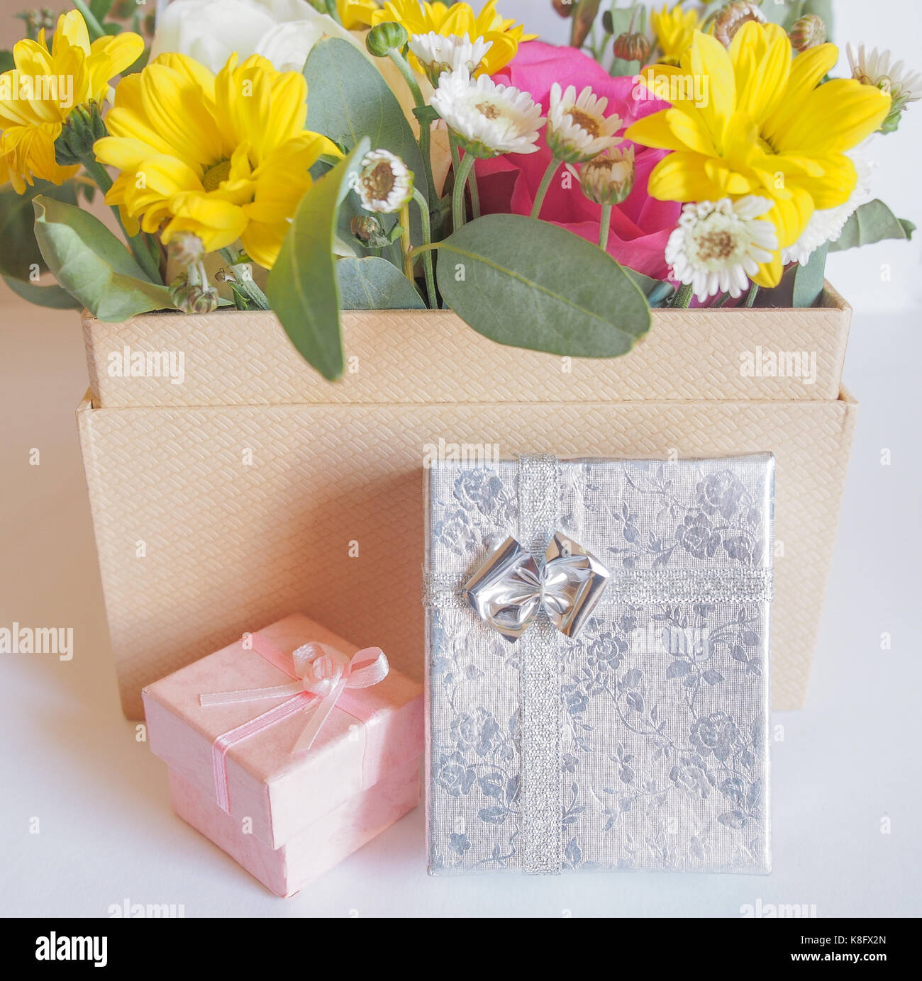 A large box holding a bouquet of flowers and two small gift boxes on a white background. Stock Photo