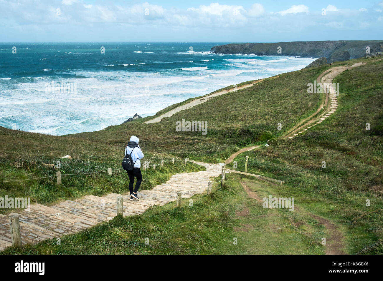 Bedruthan Steps - a lone tourist walks down the coastal footpath at Bedruthan Steps on the North Cornwall coast. Stock Photo