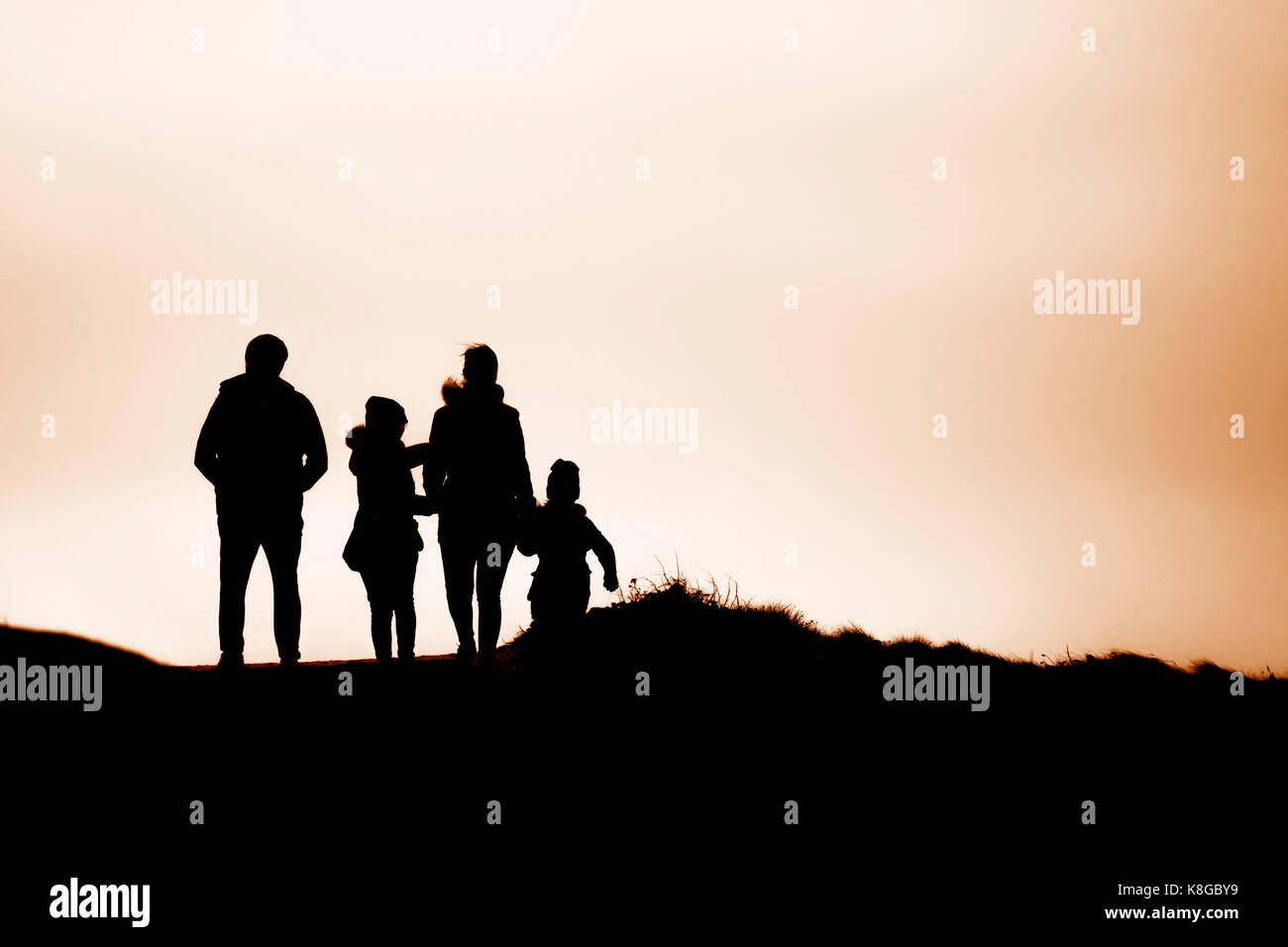 Silhouette - the silhouette of a family walking during late afternoon sunlight at Little Fistral in Newquay, Cornwall Stock Photo
