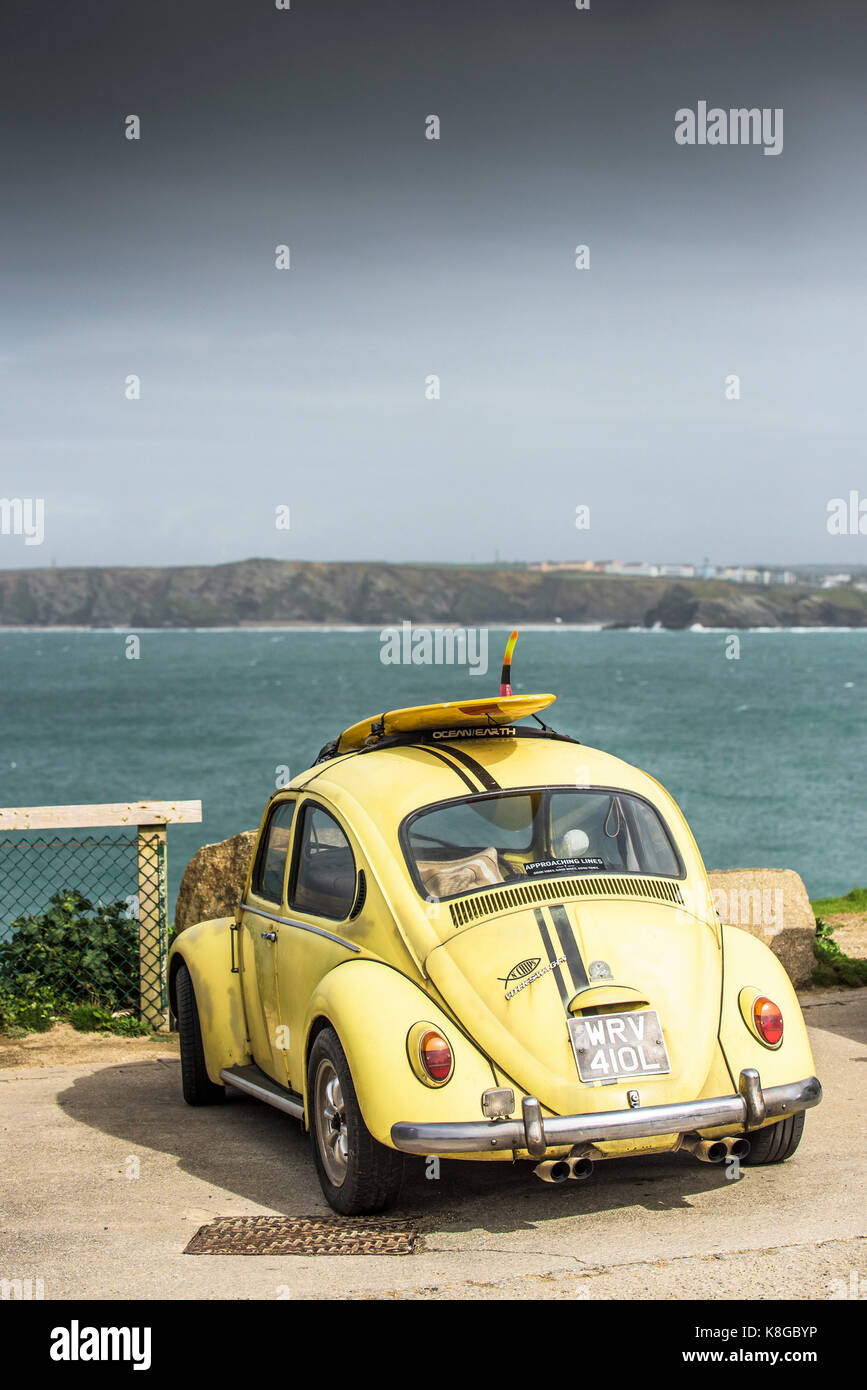 Volkswagen car - a yellow Volkswagen with a surfboard on its roof rack parked at Little Fistral in Newquay, Cornwall Stock Photo