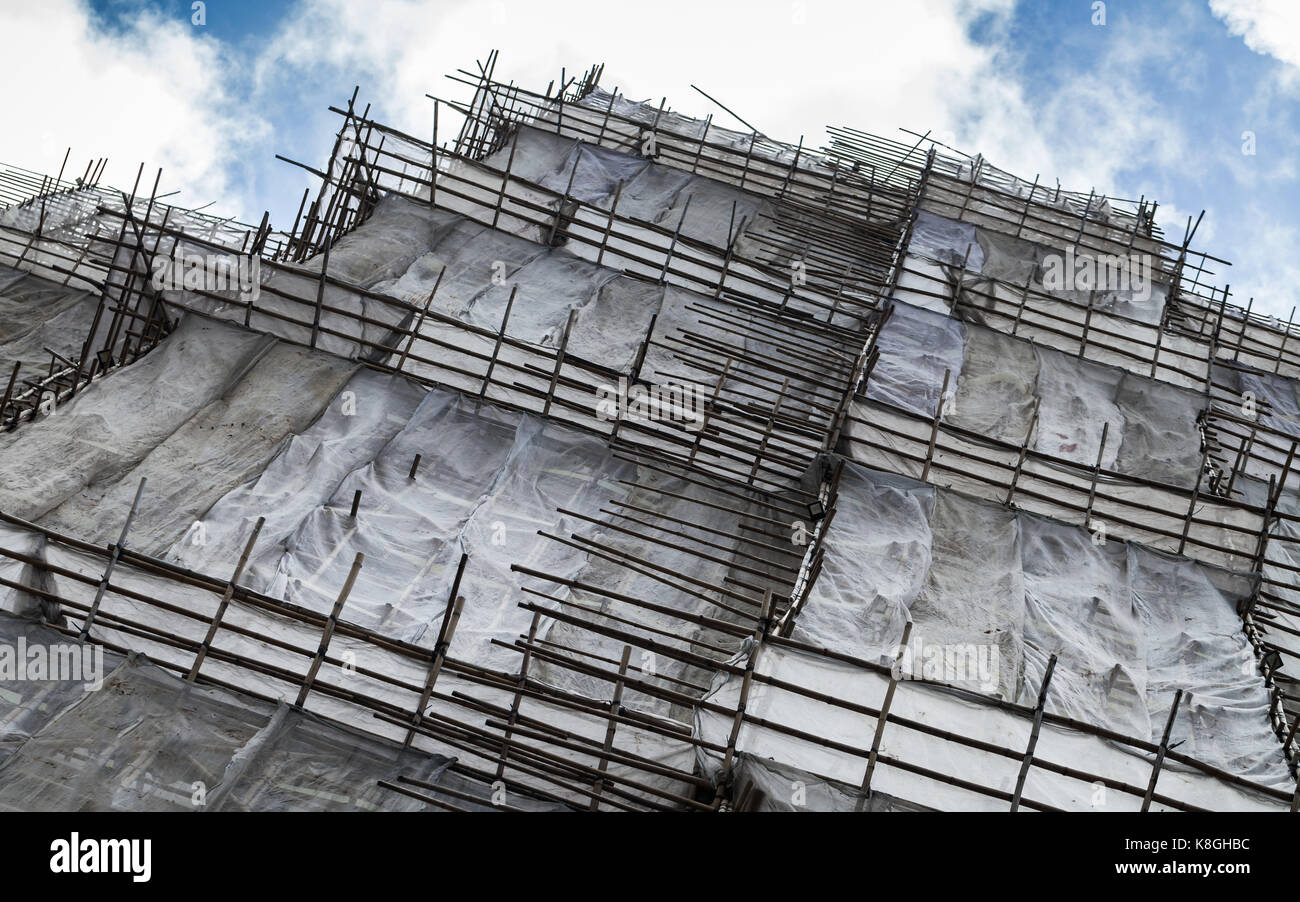 Modern block of flats is under construction, facade with protection grid and bamboo scaffolding structures, Hong Kong Stock Photo