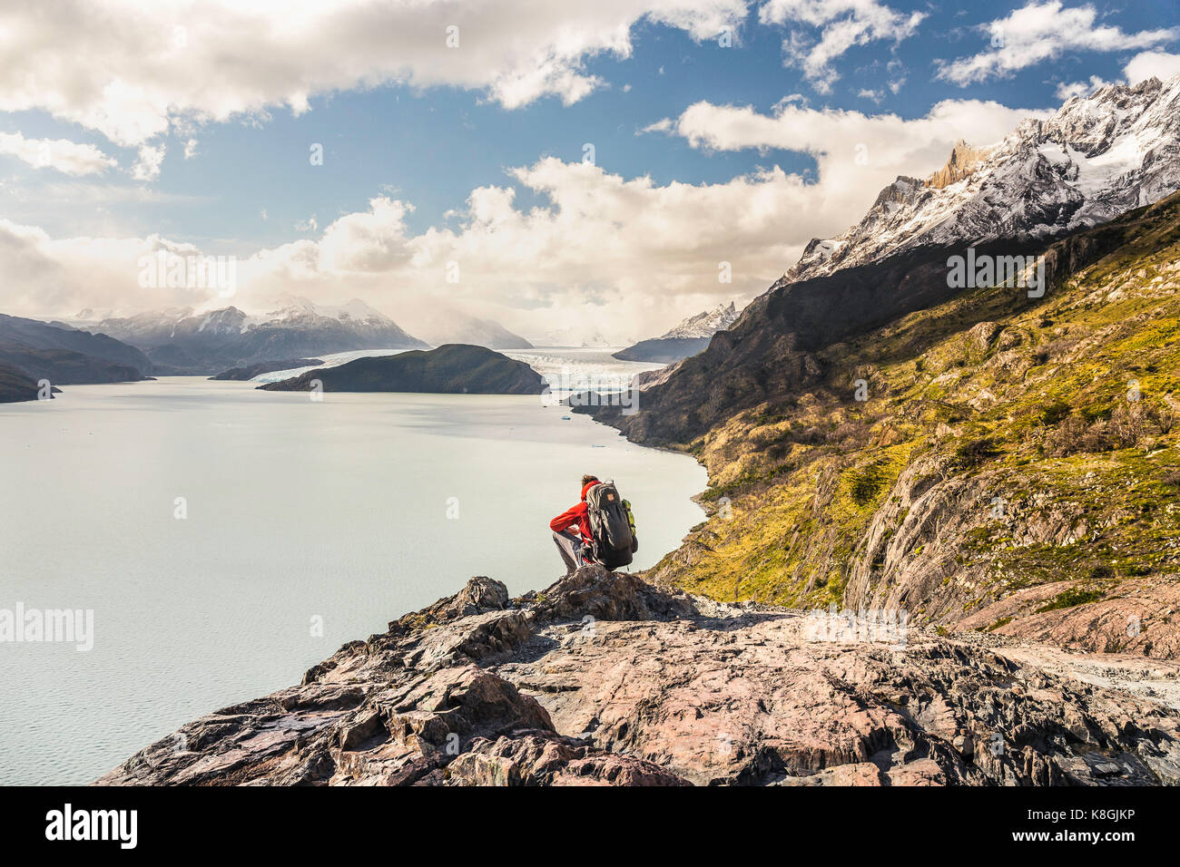 Male hiker crouching to look out over Grey Lake and Glacier, Torres del Paine national park, Chile Stock Photo