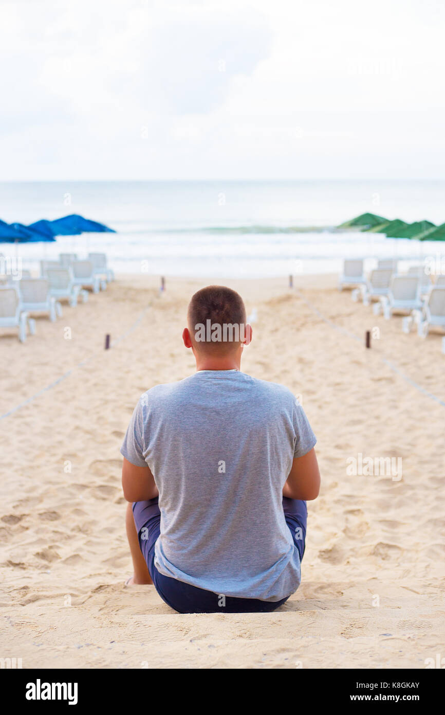 Young Guy Sits With His Back On A Sandy Beach Stock Photo