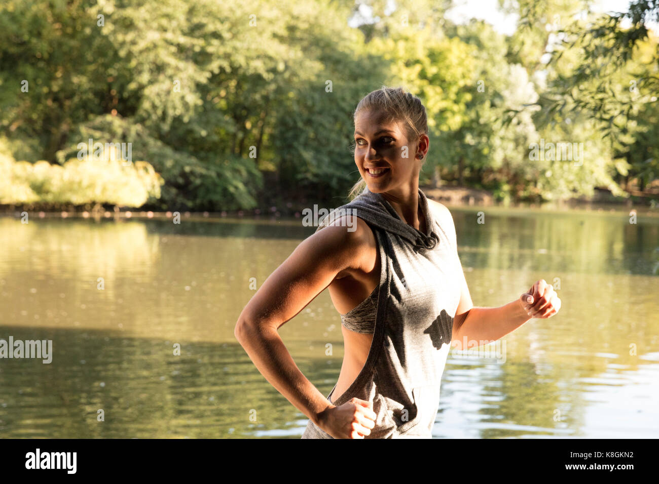 happy young female runner running by lake in park looking over her shoulder Stock Photo