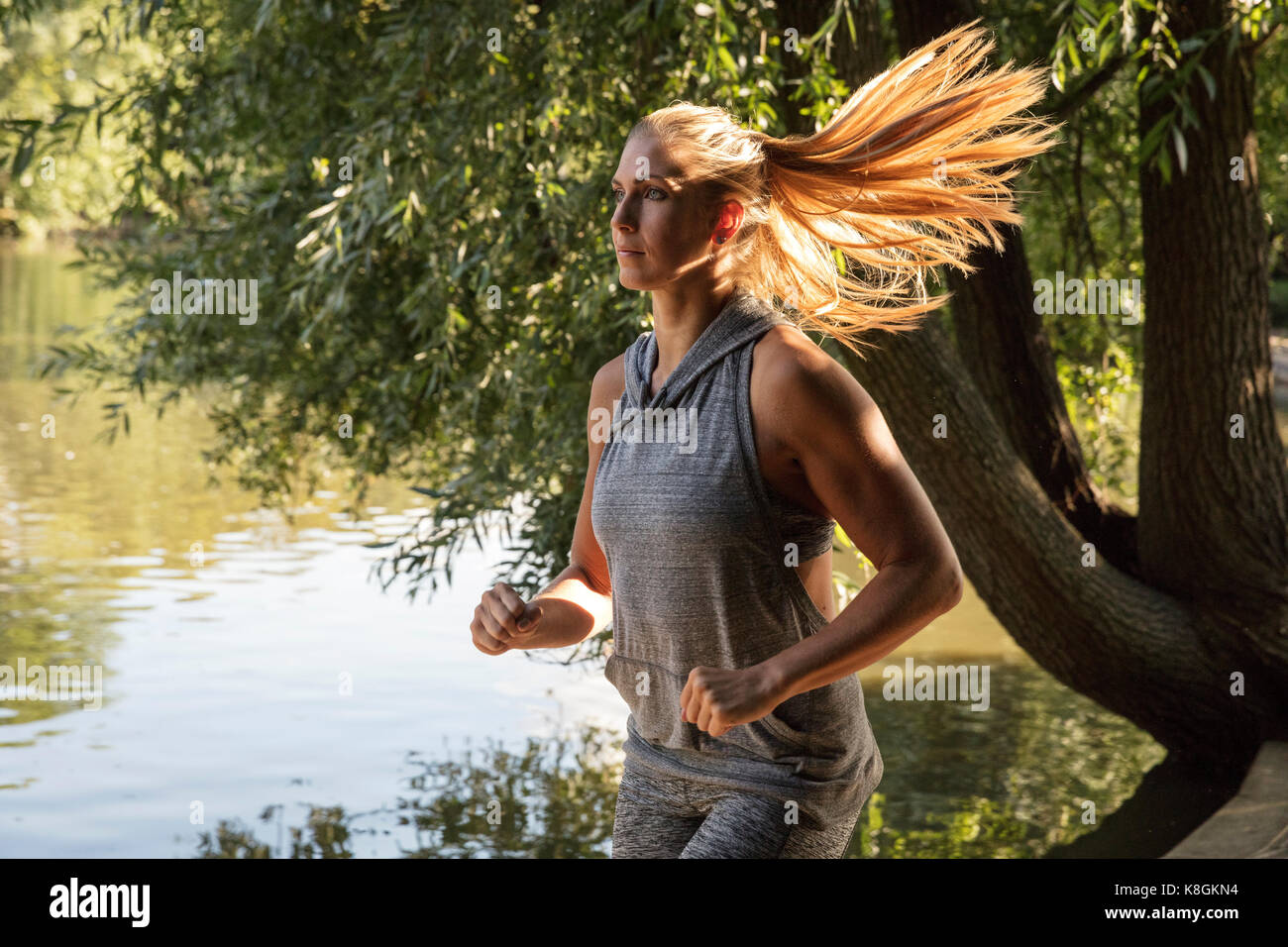 Young female runner running by park lake Stock Photo