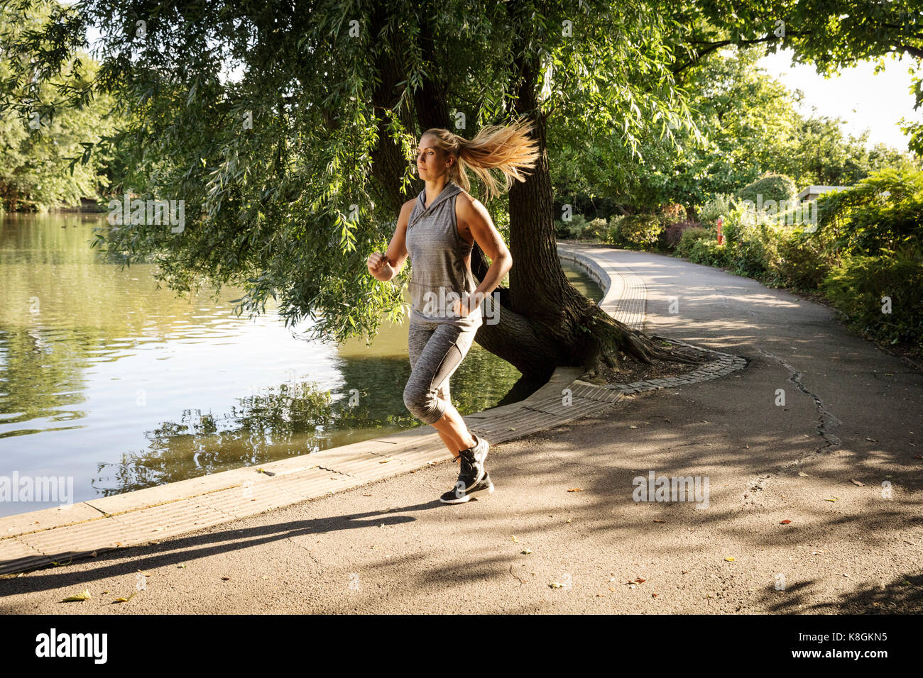 Young female runner running along park lake path Stock Photo