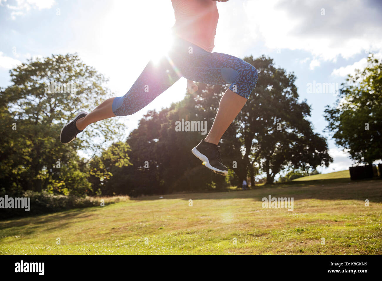 Waist down view of young woman training in park, leaping mid air in sunlight Stock Photo