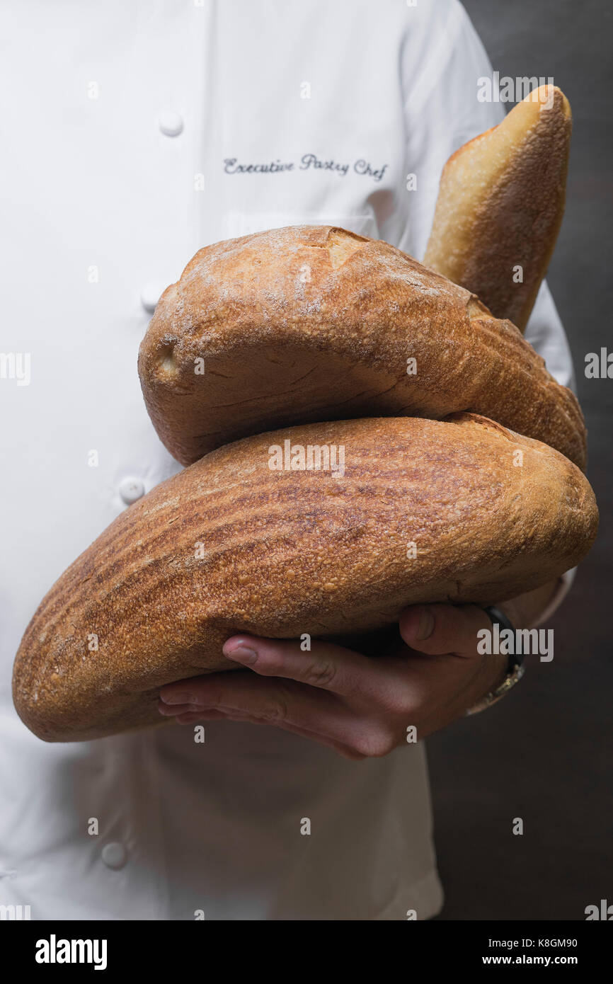 Mid section of pastry chef holding loaves in kitchen Stock Photo