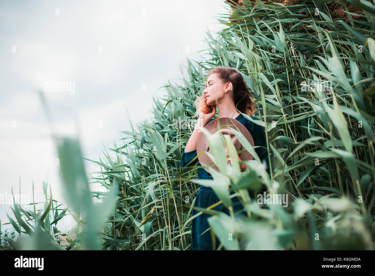 Mid adult woman beside long grass, touching hair, breathing in fresh air Stock Photo