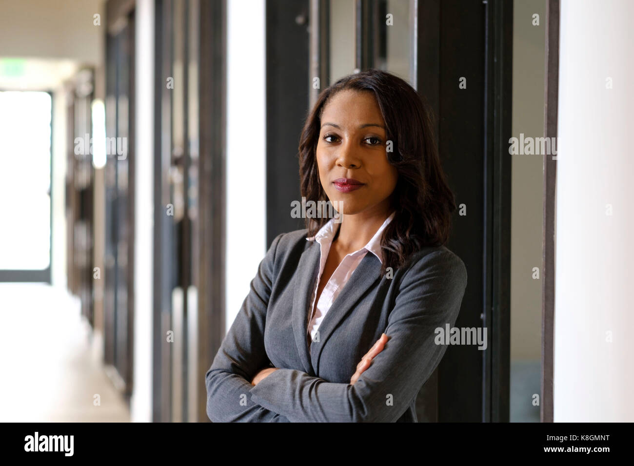 Portrait of businesswoman in office hallway, arms folded, serious expression Stock Photo