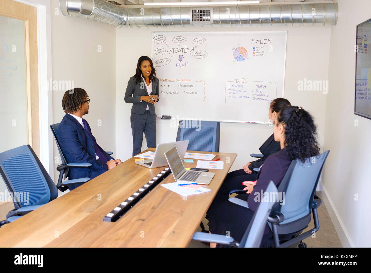 Businessman and businesswomen in meeting room, businesswoman, standing at front, explaining business strategy Stock Photo