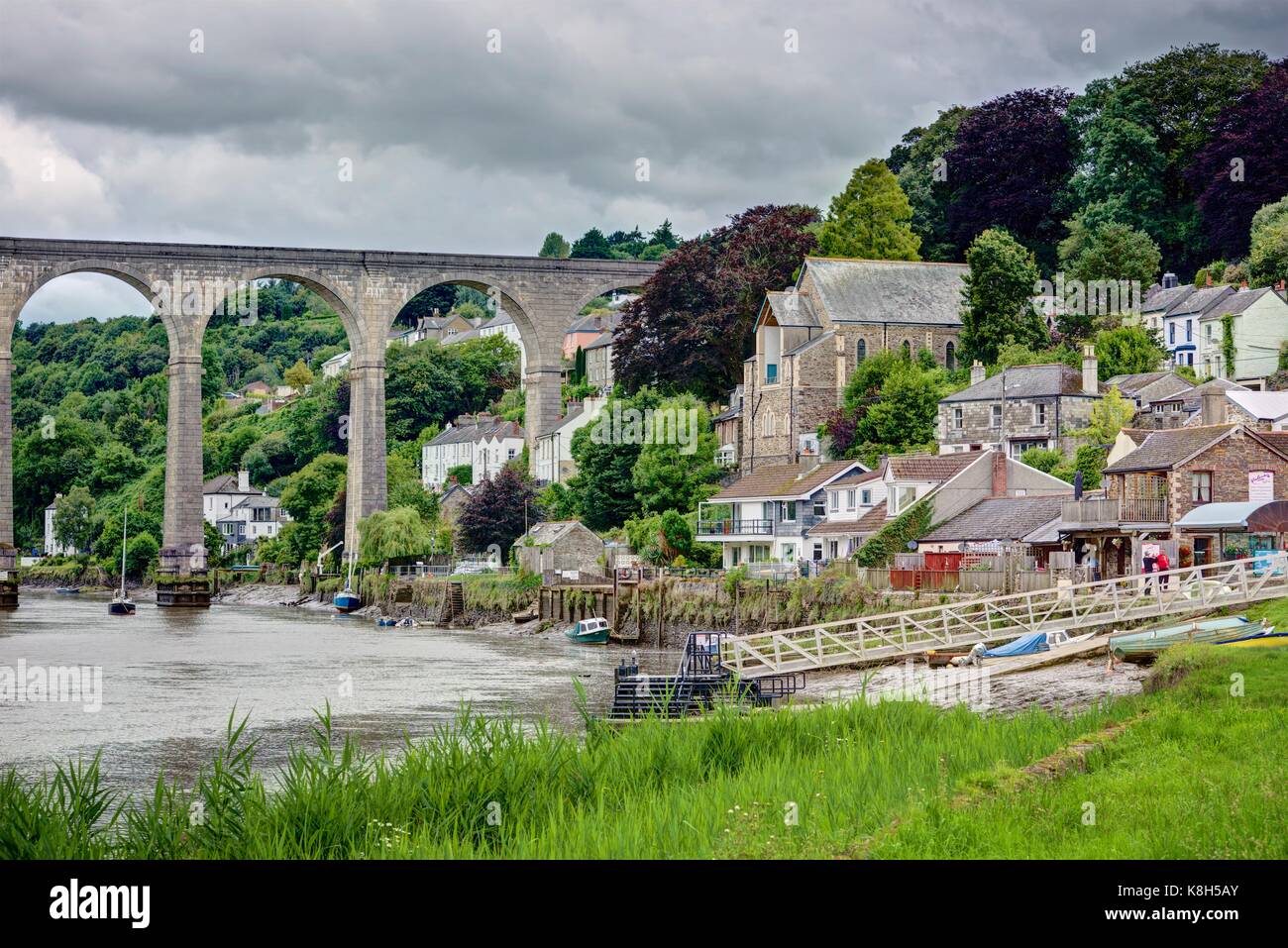 A landscape of the great stone arched Calstock Viaduct crossing the Tamar River going to sea. A green bank of grass leads you into Calstock village. Stock Photo