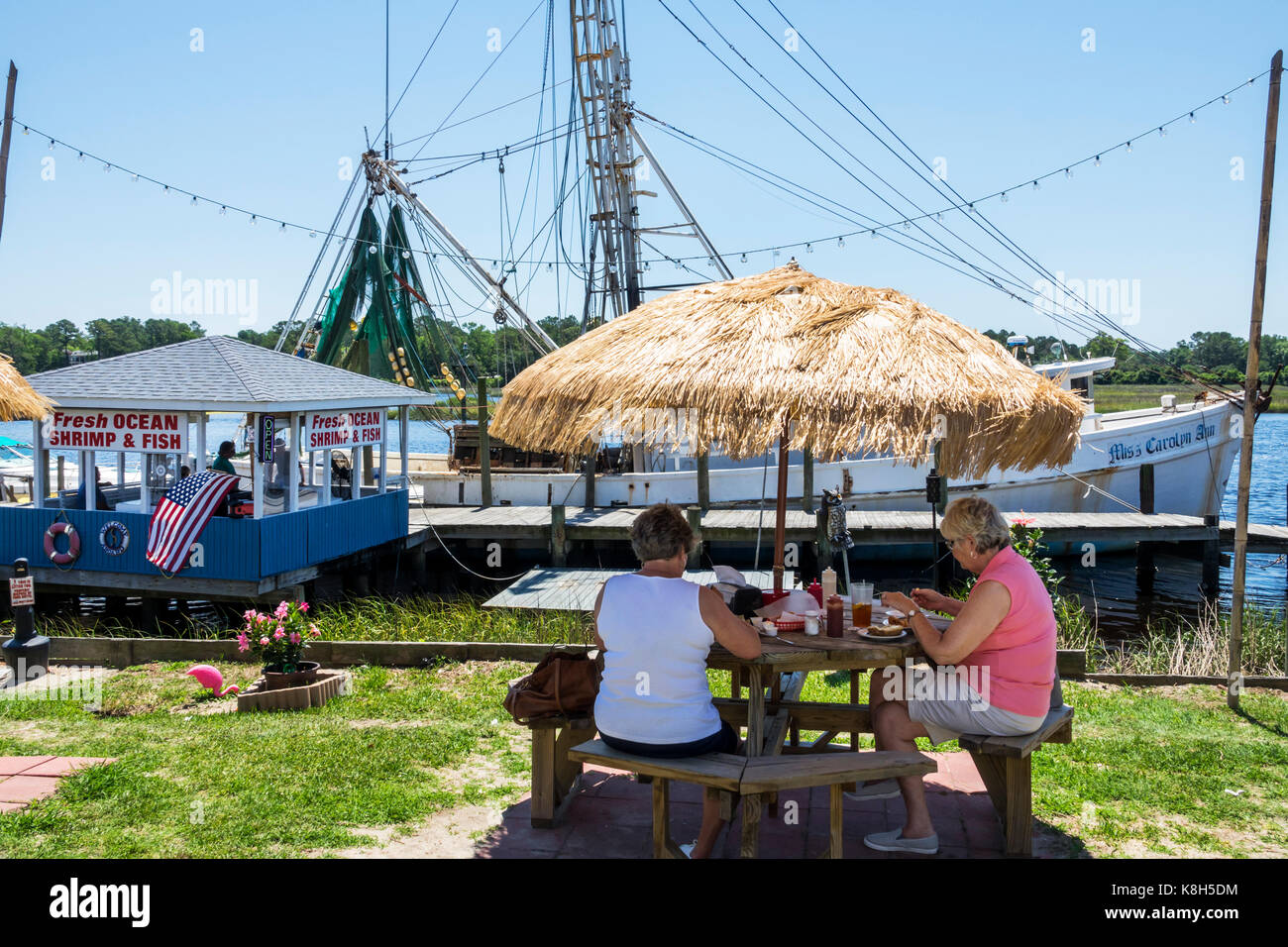 North Carolina,NC,Calabash,fishing town,seafood,regional cuisine,dining,al fresco sidewalk outside outdoors tables,straw umbrella,fishing boat,dock,Ca Stock Photo