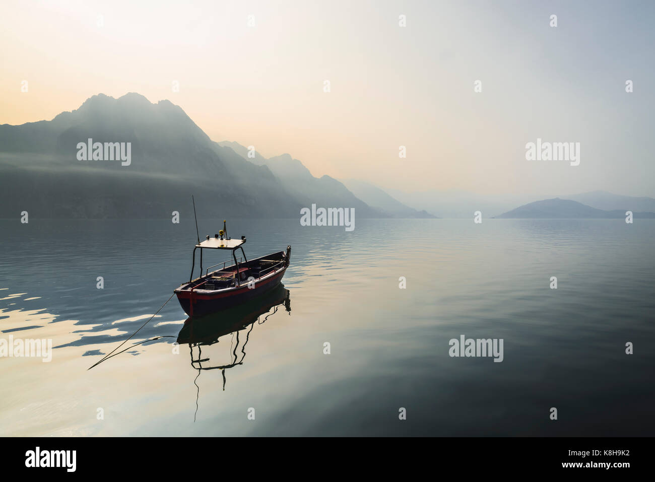Panorama of a small boat on calm Lake Iseo in front of hazy mountains and Monte Isola in the morning sun, Lombardy, Italy Stock Photo