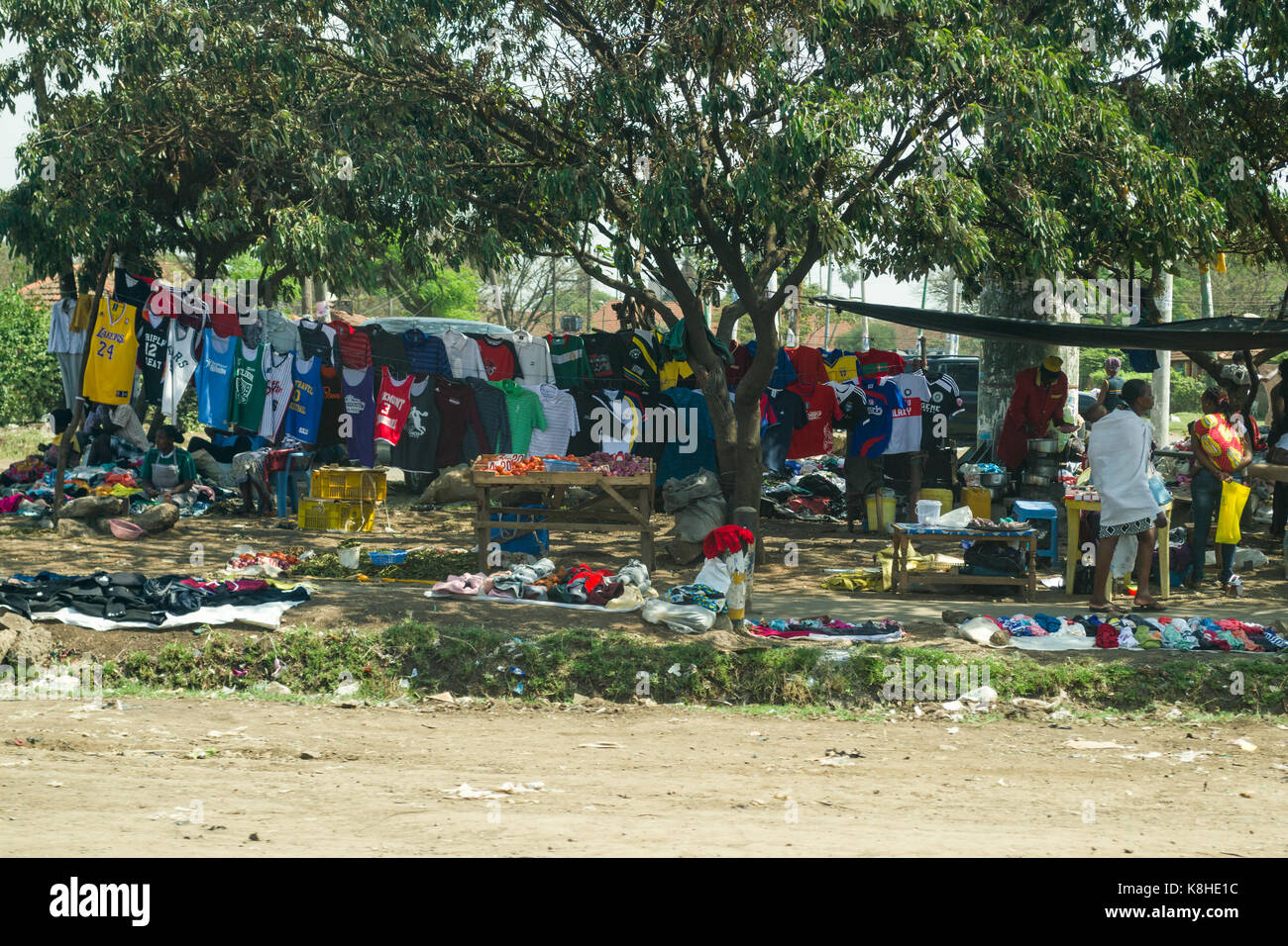 Clothes  hanging in shade and on ground on display under tree by roadside with people looking, Nairobi, Kenya Stock Photo