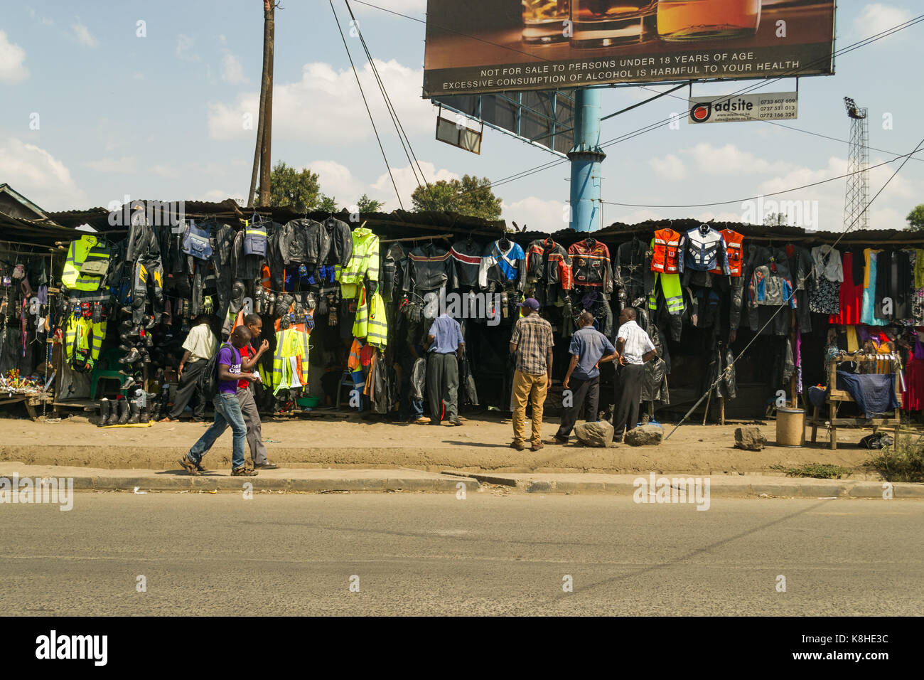 Various roadside stalls selling motorbike and bicycle clothing with people looking, Nairobi, Kenya Stock Photo