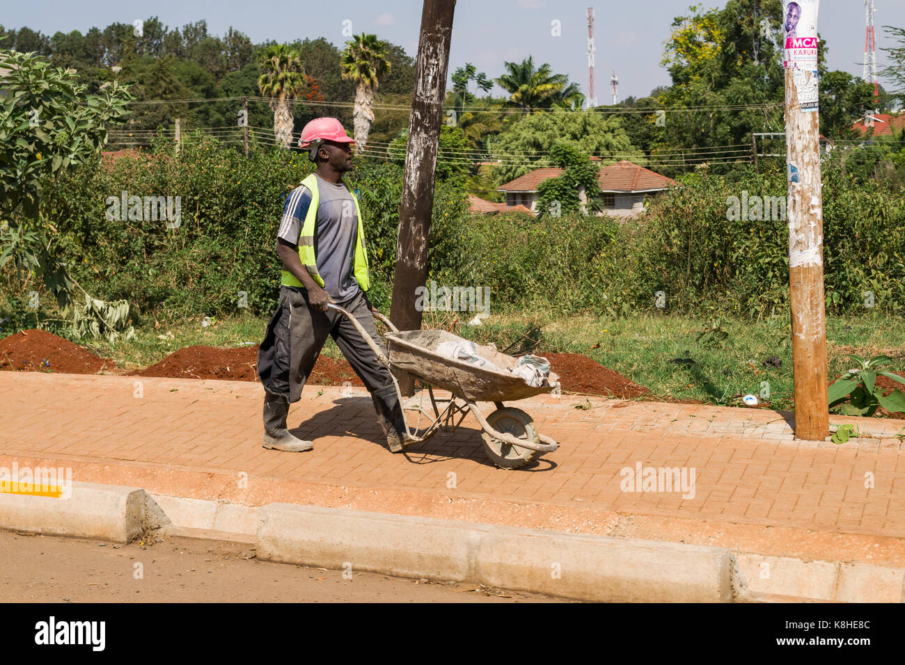 Construction worker walking pushing wheelbarrow on pavement, Nairobi, Kenya Stock Photo