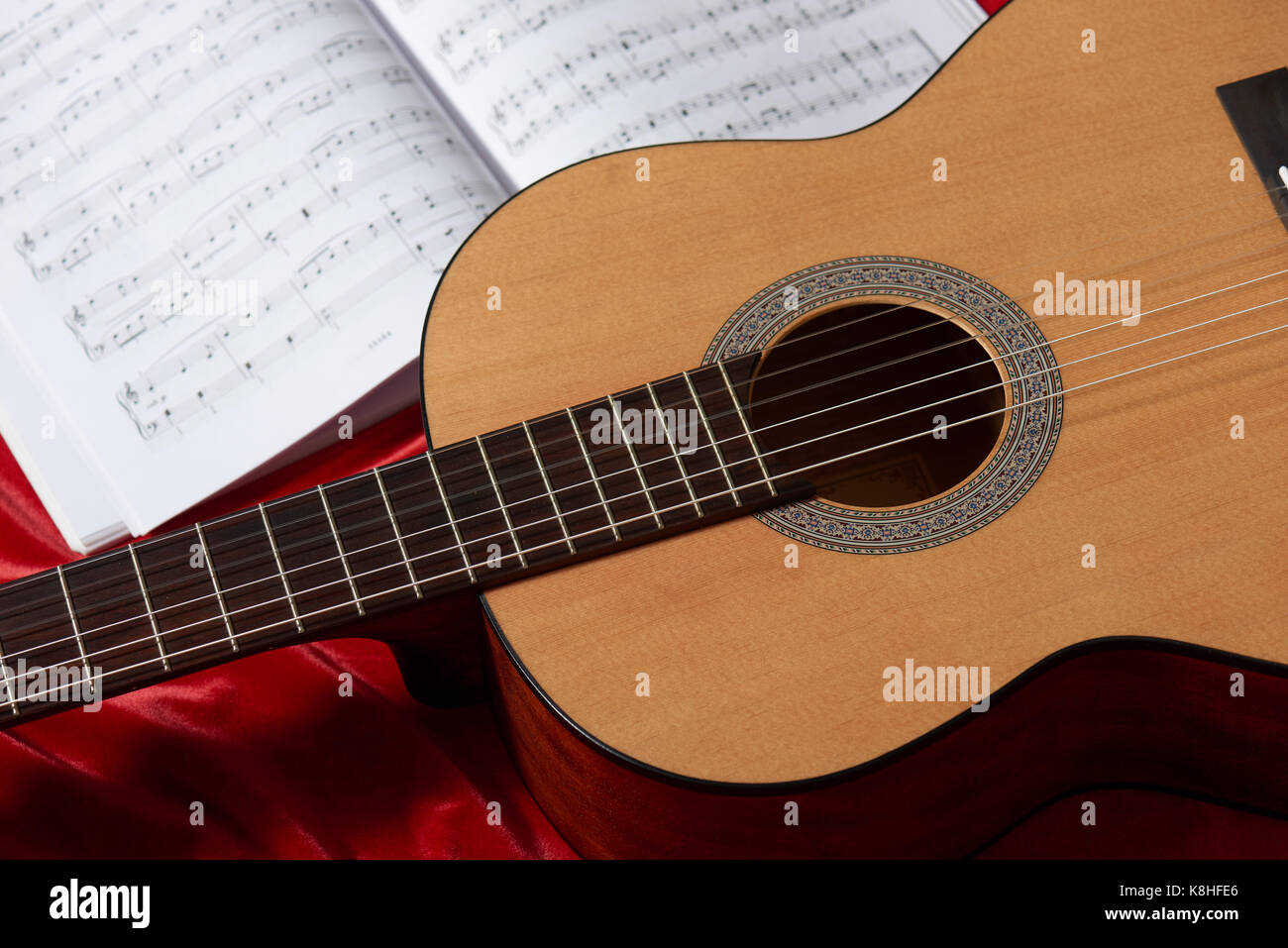 acoustic guitar and music notes on red fabric, close view of objects ...