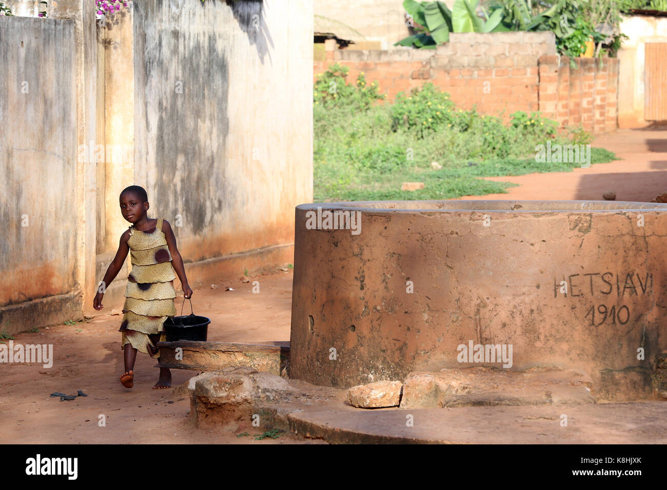 African village life. girl with water close to a well. togoville. togo. Stock Photo