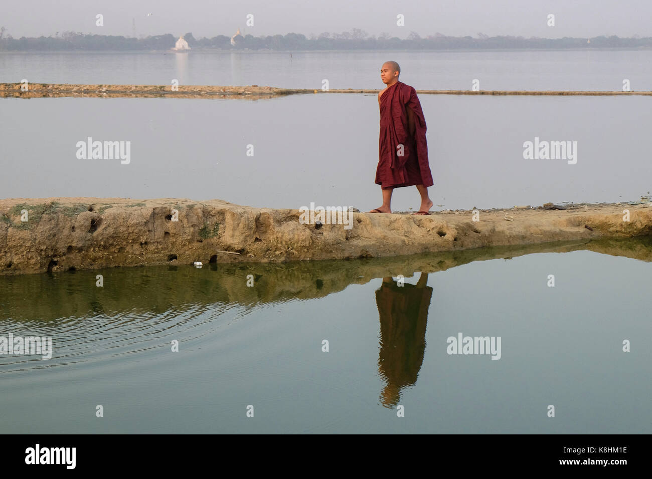 Burma, Myanmar, Mandalay: monk walking on a path leading to Taungthaman Lake Stock Photo