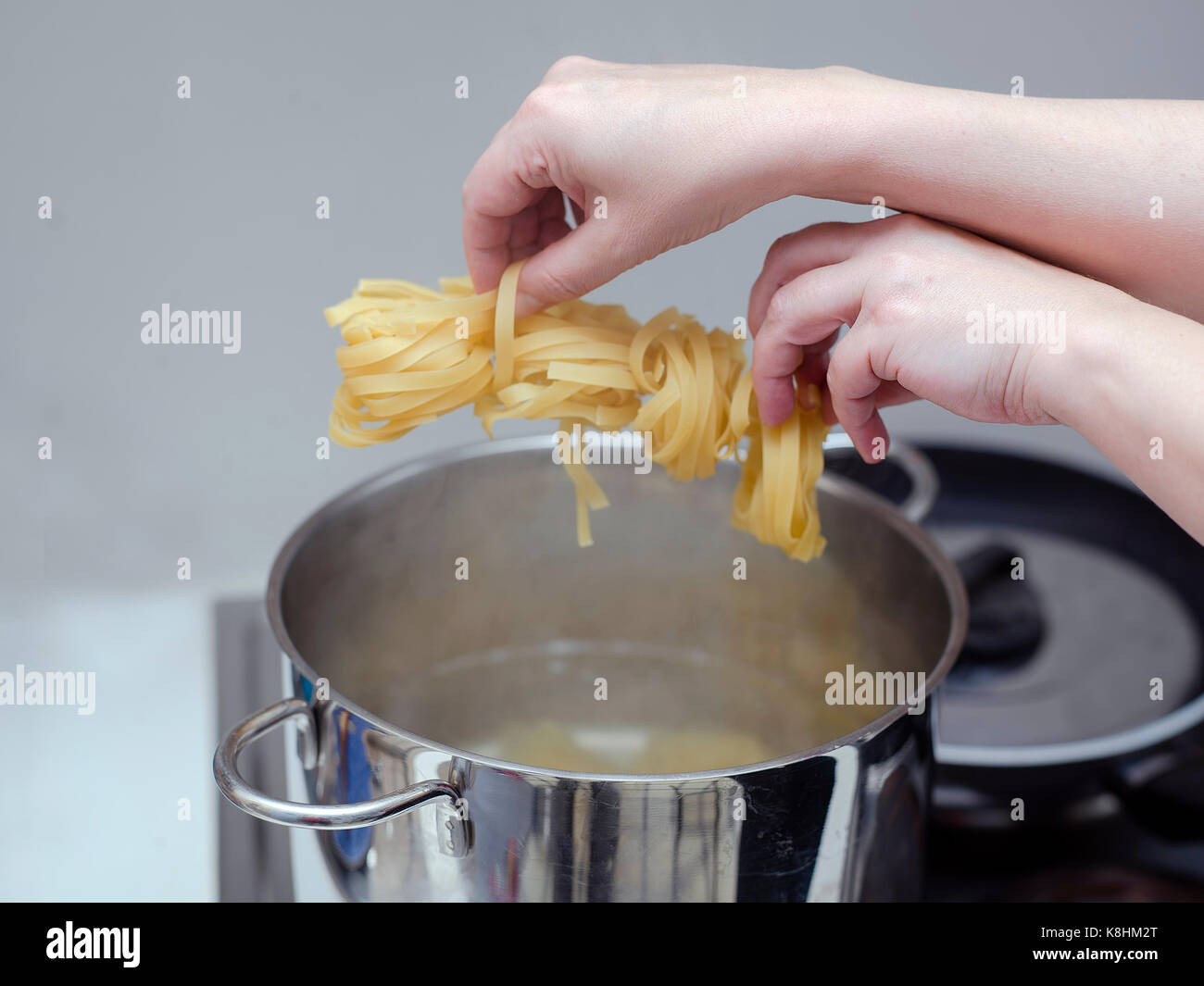 Female hands about to drop spaghetti into a boiling water, the steam coming out of casserole Stock Photo