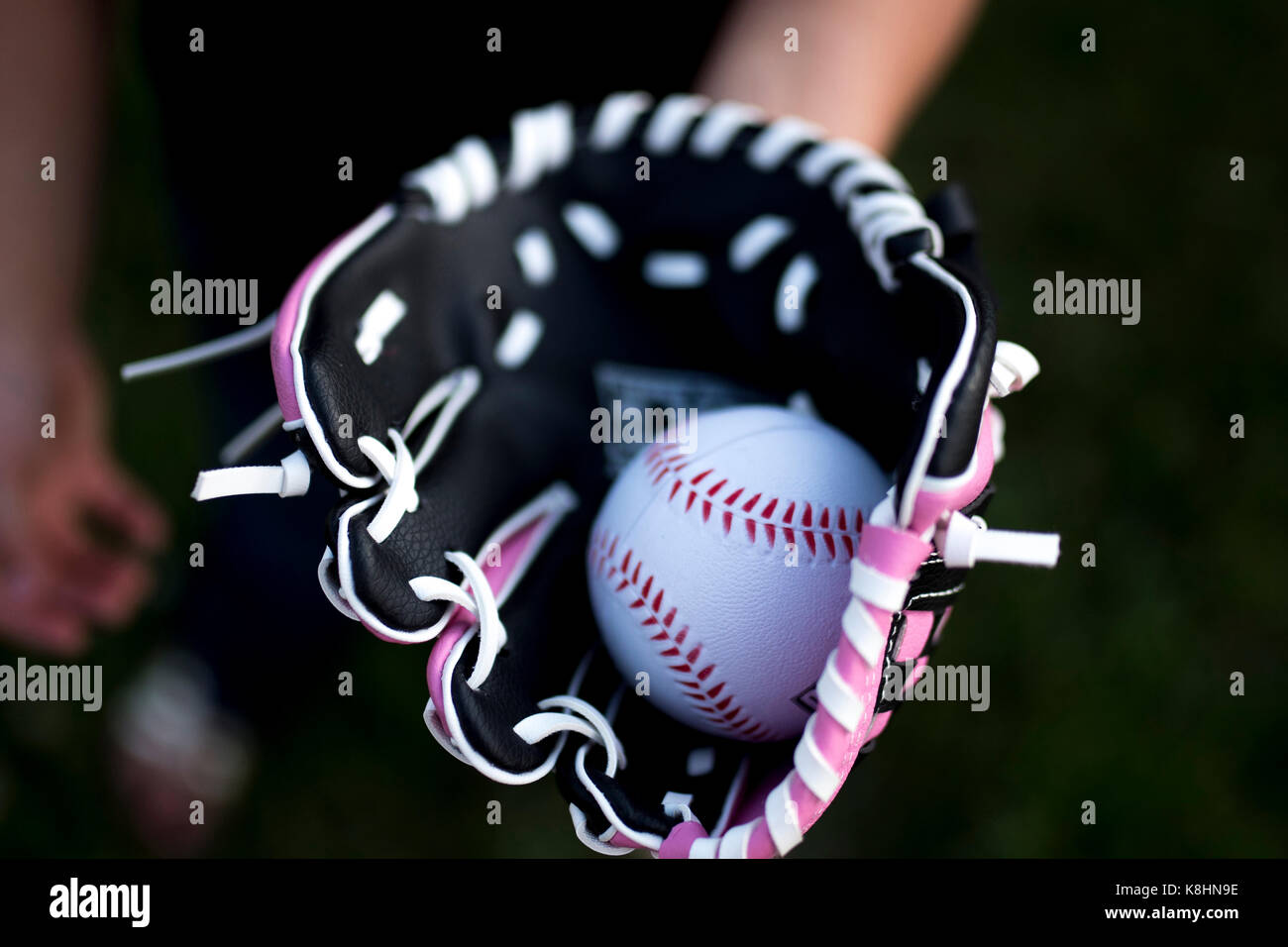 Cropped hand of girl wearing baseball glove with ball Stock Photo