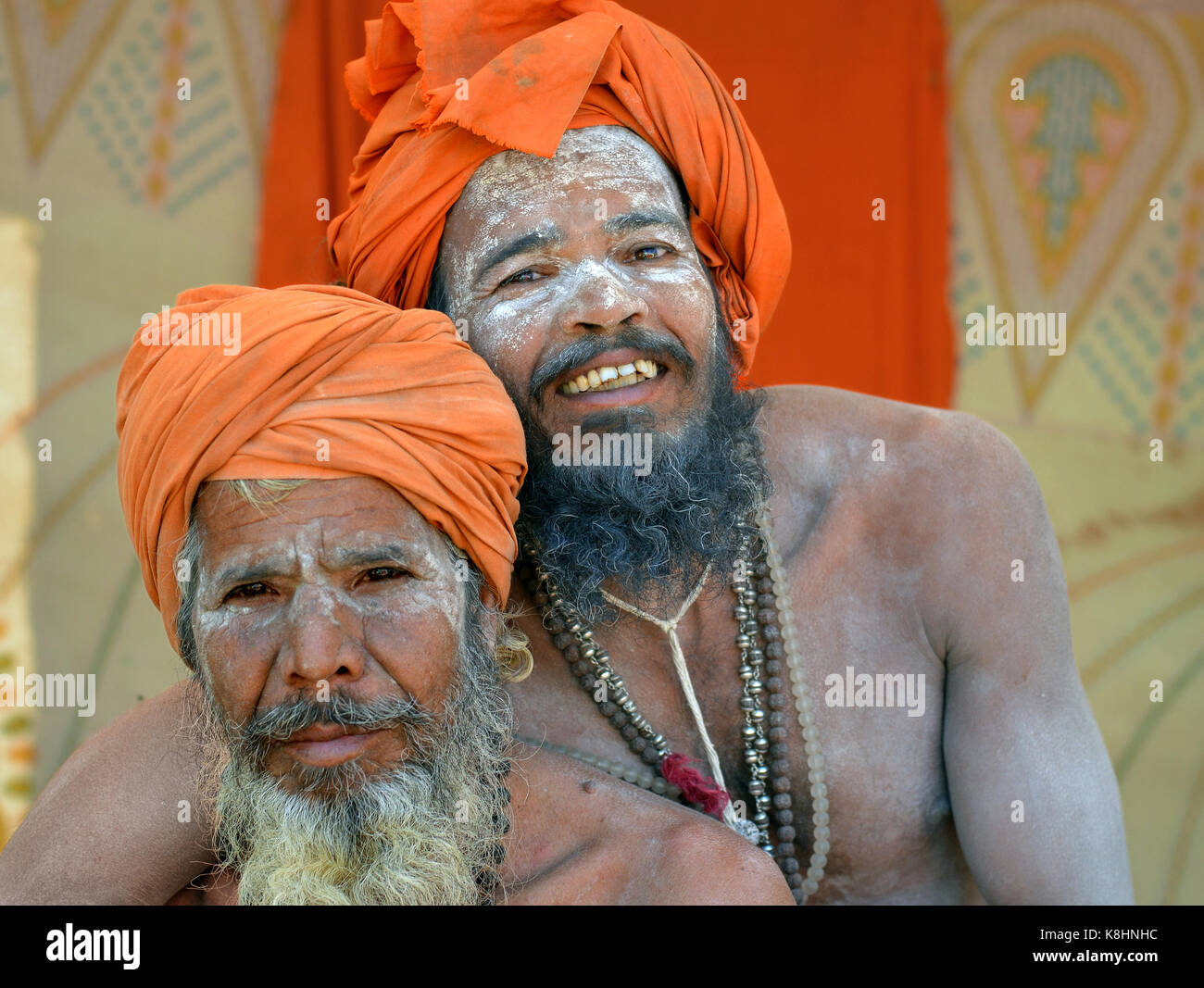 Two happy Indian Hindu sadhus with orange turbans and sacred white ash all over their faces, beards and bodies, hugging each other in a close embrace Stock Photo