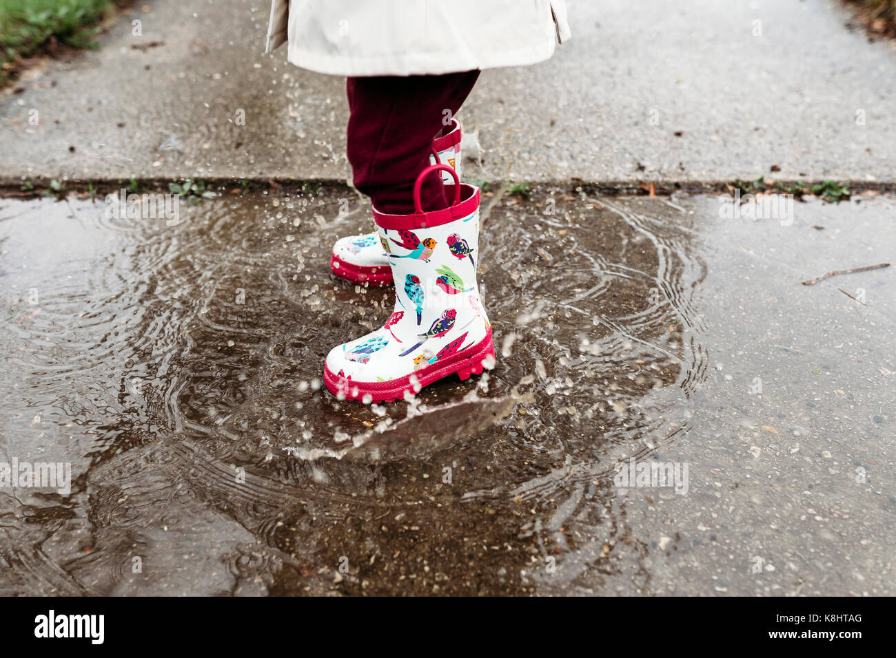 Low section of girl wearing rubber boots while standing in puddle Stock ...