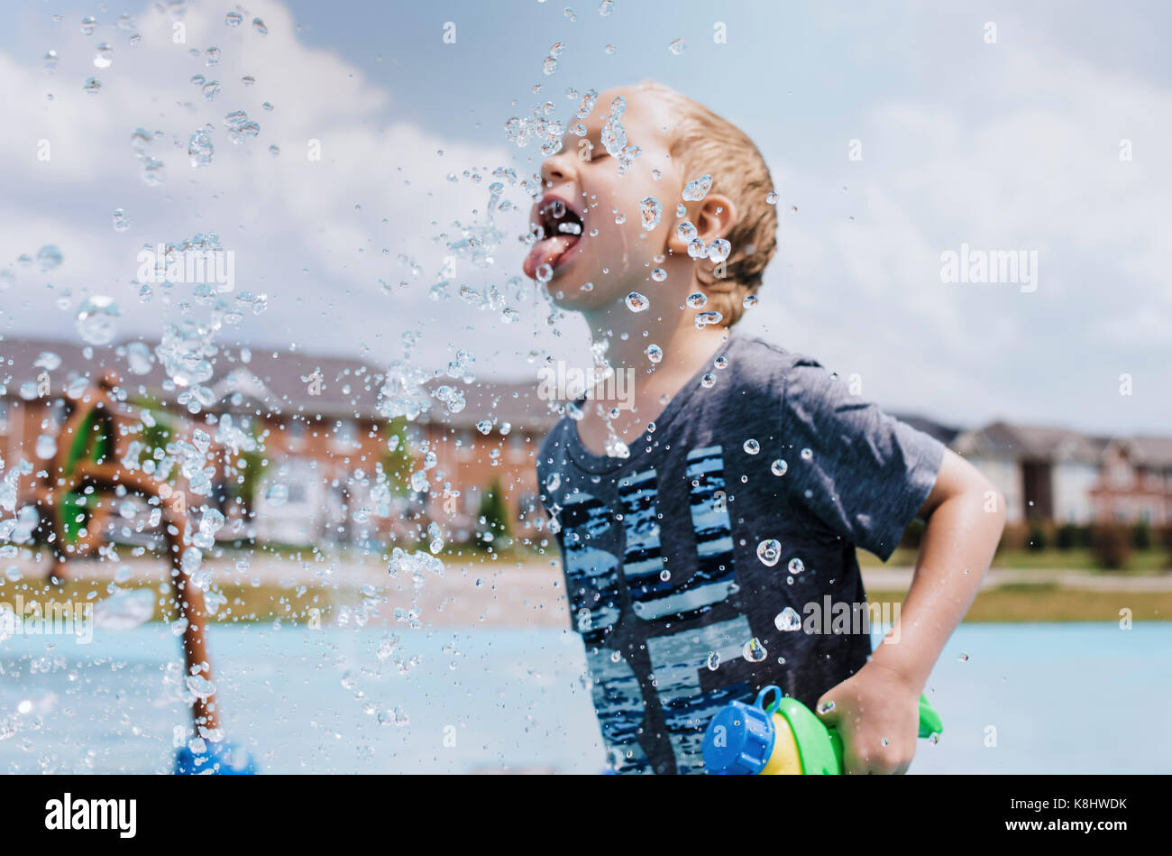 Playful boy sticking out tongue while standing spraying water Stock Photo