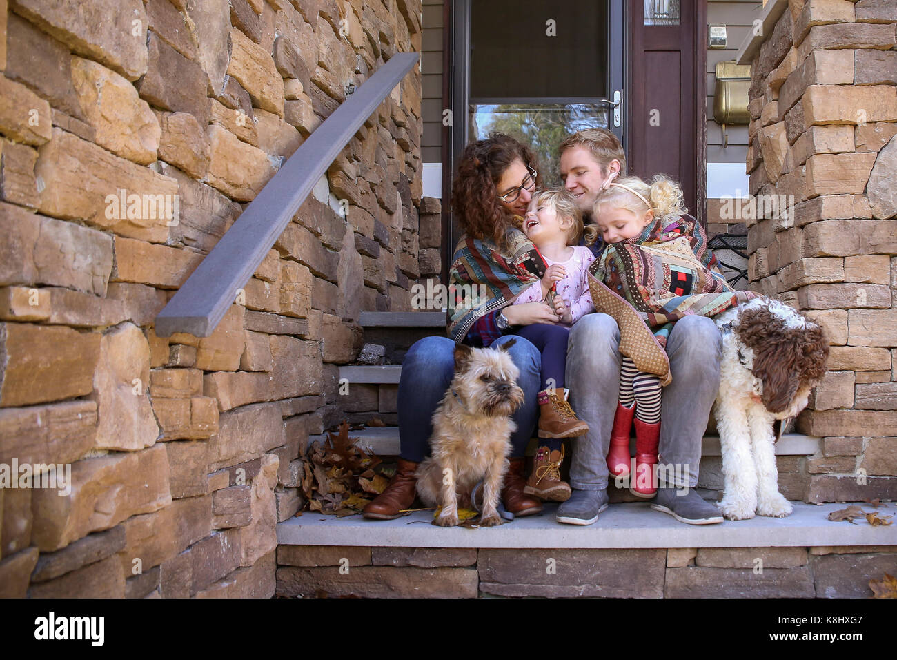 Happy family wrapped in blanket with dogs sitting on steps against house Stock Photo