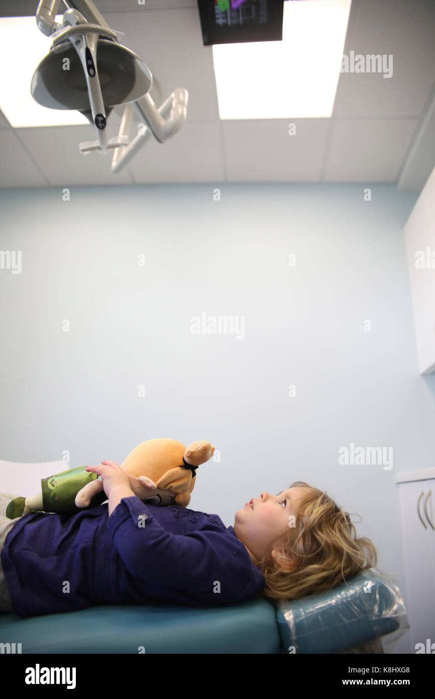 Girl with toy lying on hospital bed looking at equipment in ceiling Stock Photo