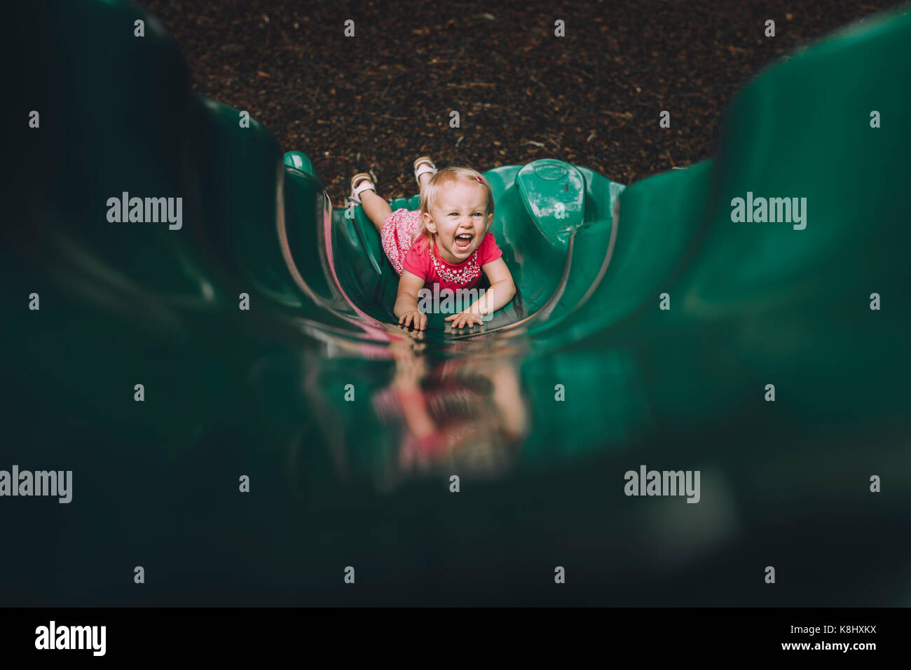 High angle portrait of happy baby girl playing on slide at playground ...