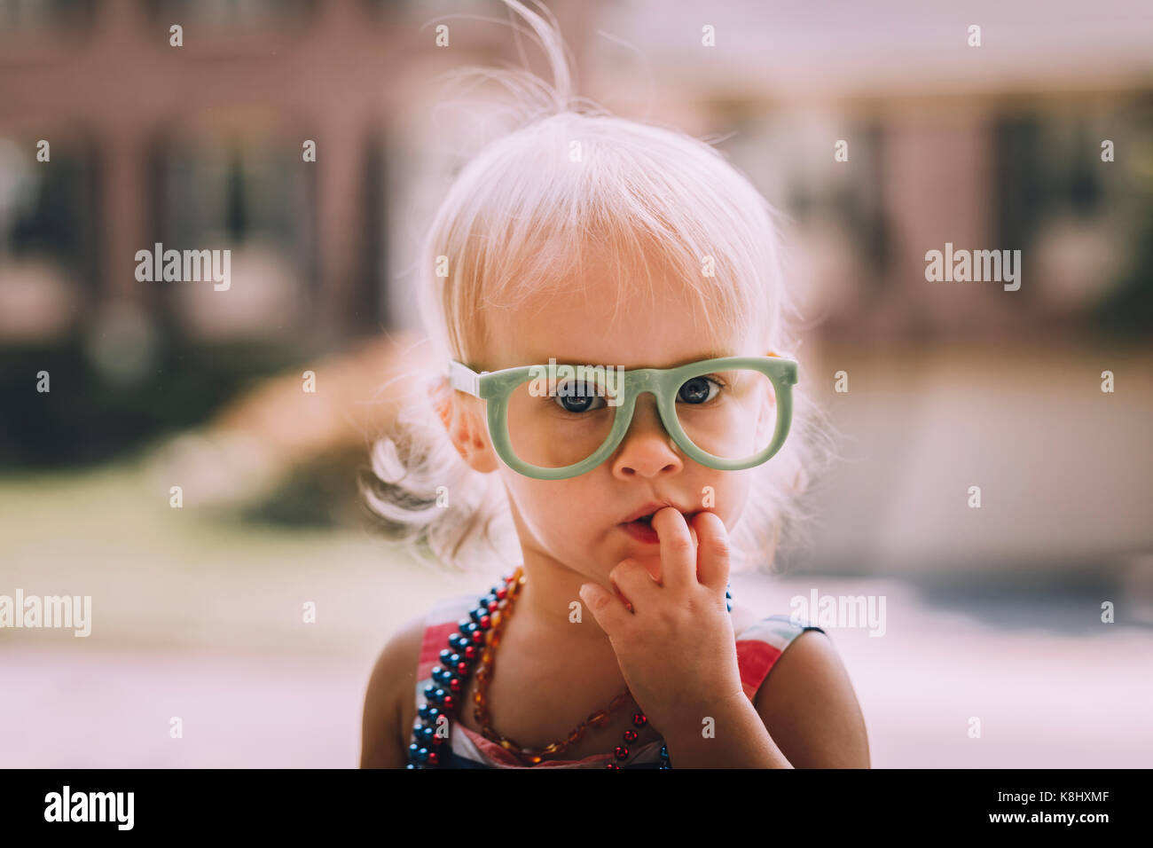 Portrait of cute baby girl wearing eyeglasses with finger in mouth Stock Photo