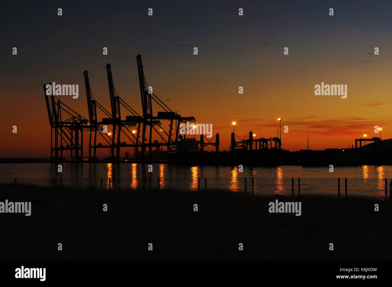 Row of cranes of the port of Malaga in the sunset reflecting in sea water Stock Photo